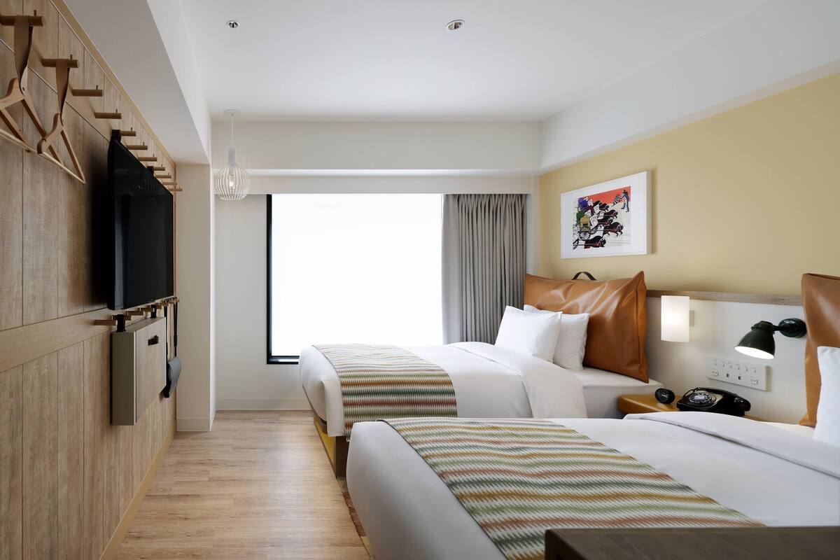 Une chambre d’hôtel avec deux lits, une télévision, un bureau avec une lampe et une fenêtre avec des rideaux.
