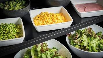 A variety of food items including broccoli, corn, edamame, cherry tomatoes, and lettuce arranged on a table.