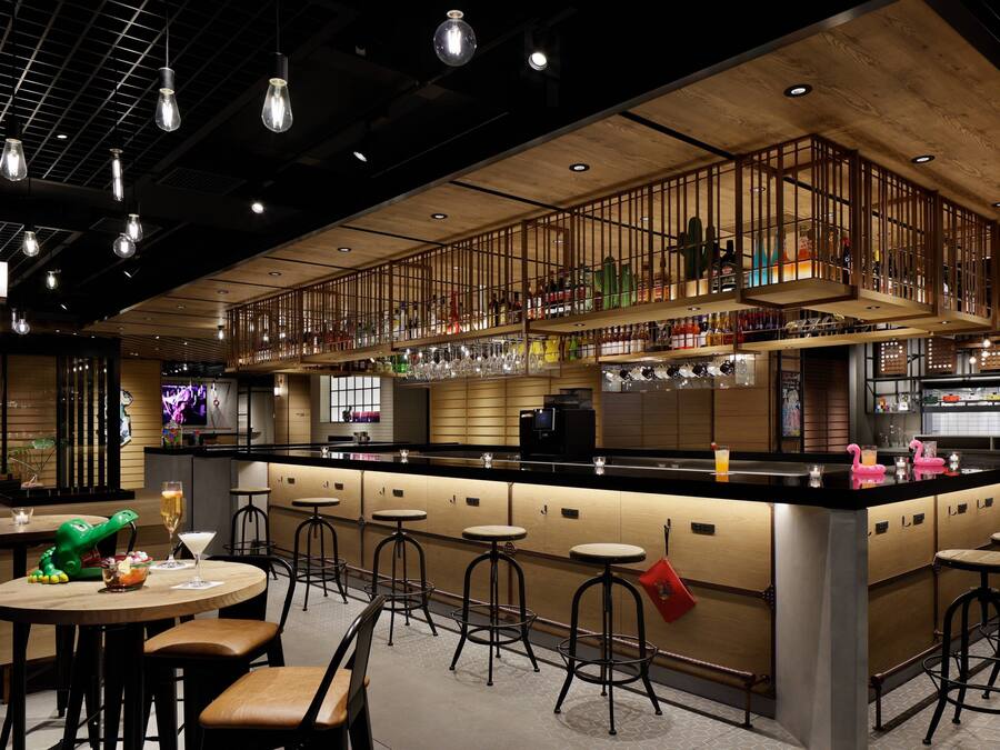 A bar area with stools, a counter, and a variety of bottles and glasses.