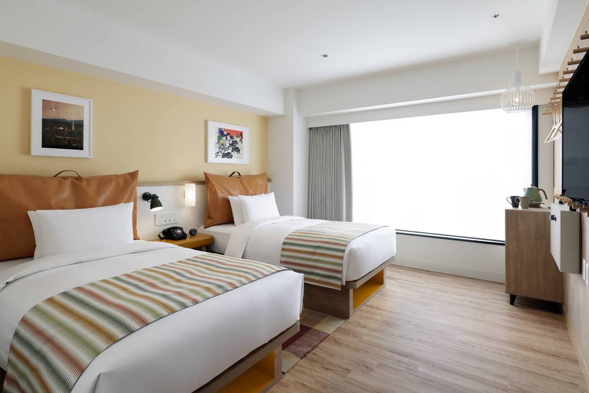 Une chambre d’hôtel avec deux lits, une grande fenêtre, un téléviseur à écran plat et une armoire en bois.