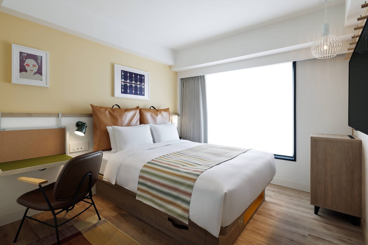 Une chambre d’hôtel moderne équipée d’un lit, d’un bureau, d’une chaise et d’une grande fenêtre.