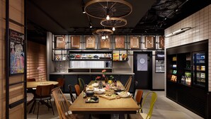 A modern dining area with a wooden table, chairs, and a kitchen in the background. - Moxy Kyoto (Kyoto)