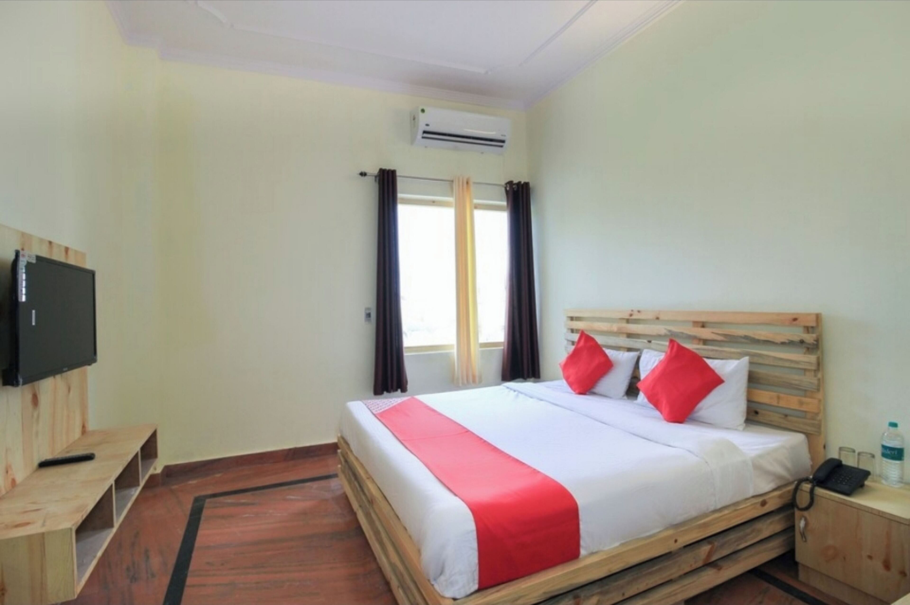 A hotel room with a wooden bed, a TV on a wooden stand, a bedside table, and a window with curtains.