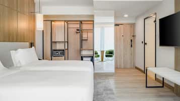A modern hotel room with a large bed, a TV, a walk-in closet, and a view of the outdoors.