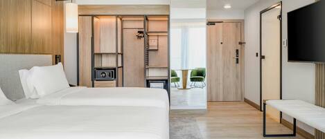 Habitación de hotel moderna con una cama grande, televisión, vestidor y vistas al exterior.