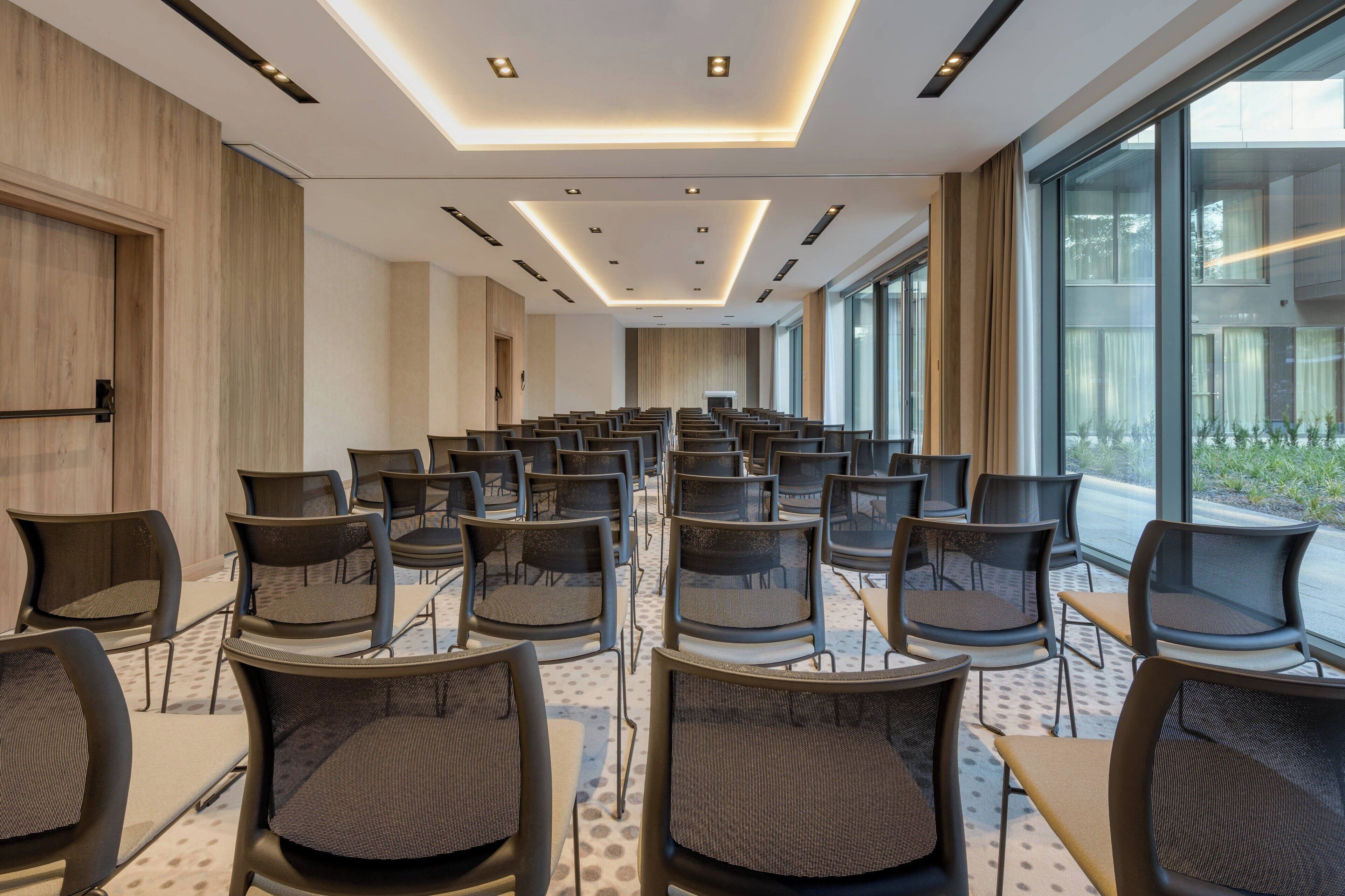 Une salle de conférence avec des rangées de chaises et de tables, de grandes fenêtres et un design moderne au niveau du plafond.