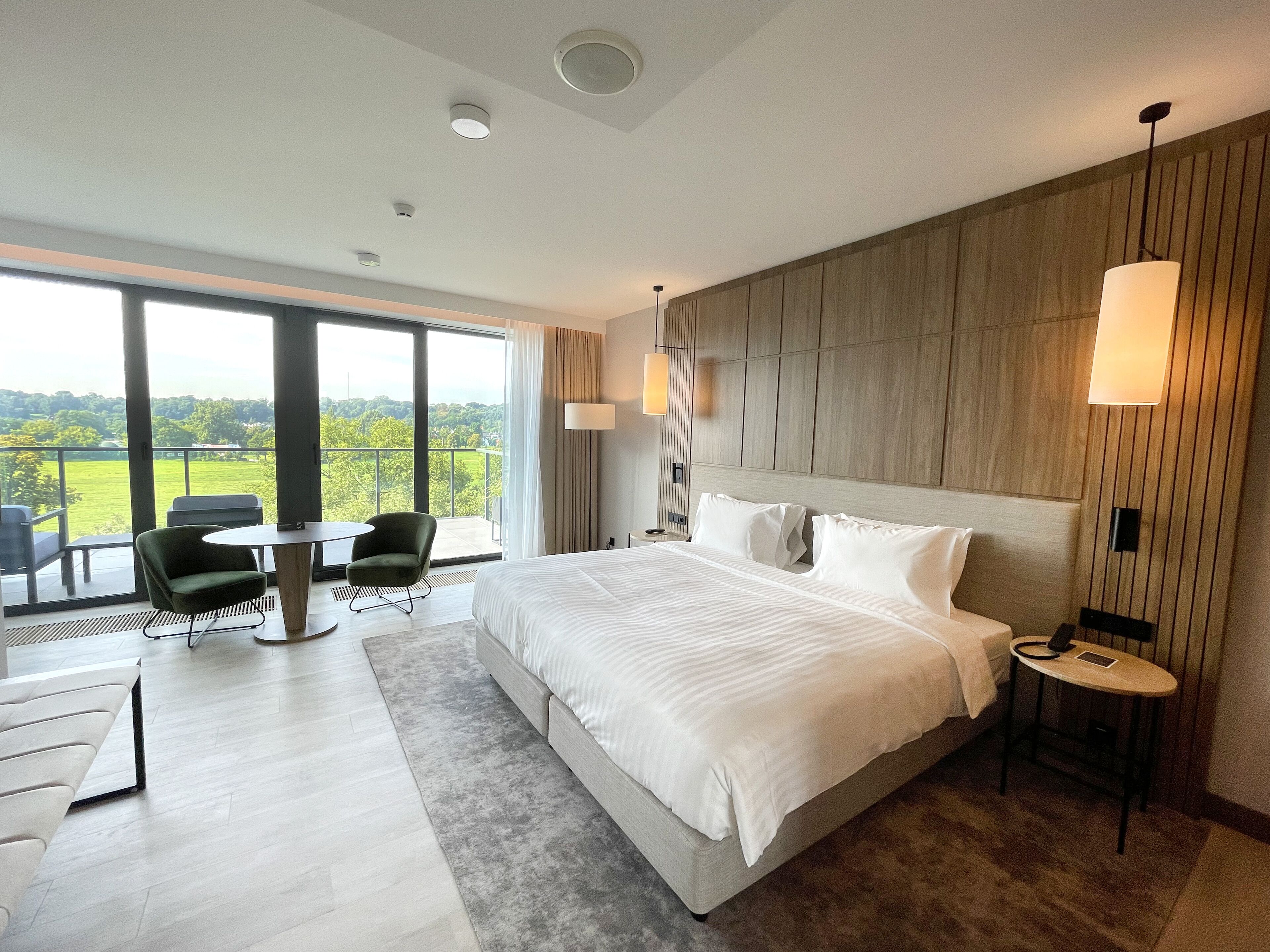 Een moderne hotelkamer met een groot bed, een bureau en een stoel. Er is een balkon met uitzicht op het landschap.