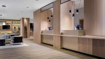 A modern hotel lobby with a wooden reception desk, a sofa, and a dining area.
