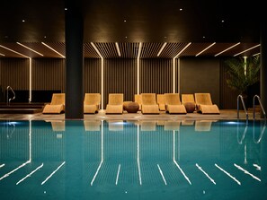 Ein moderner Poolbereich im Innenbereich mit Liegestühlen und einem Reflexionsbecken.