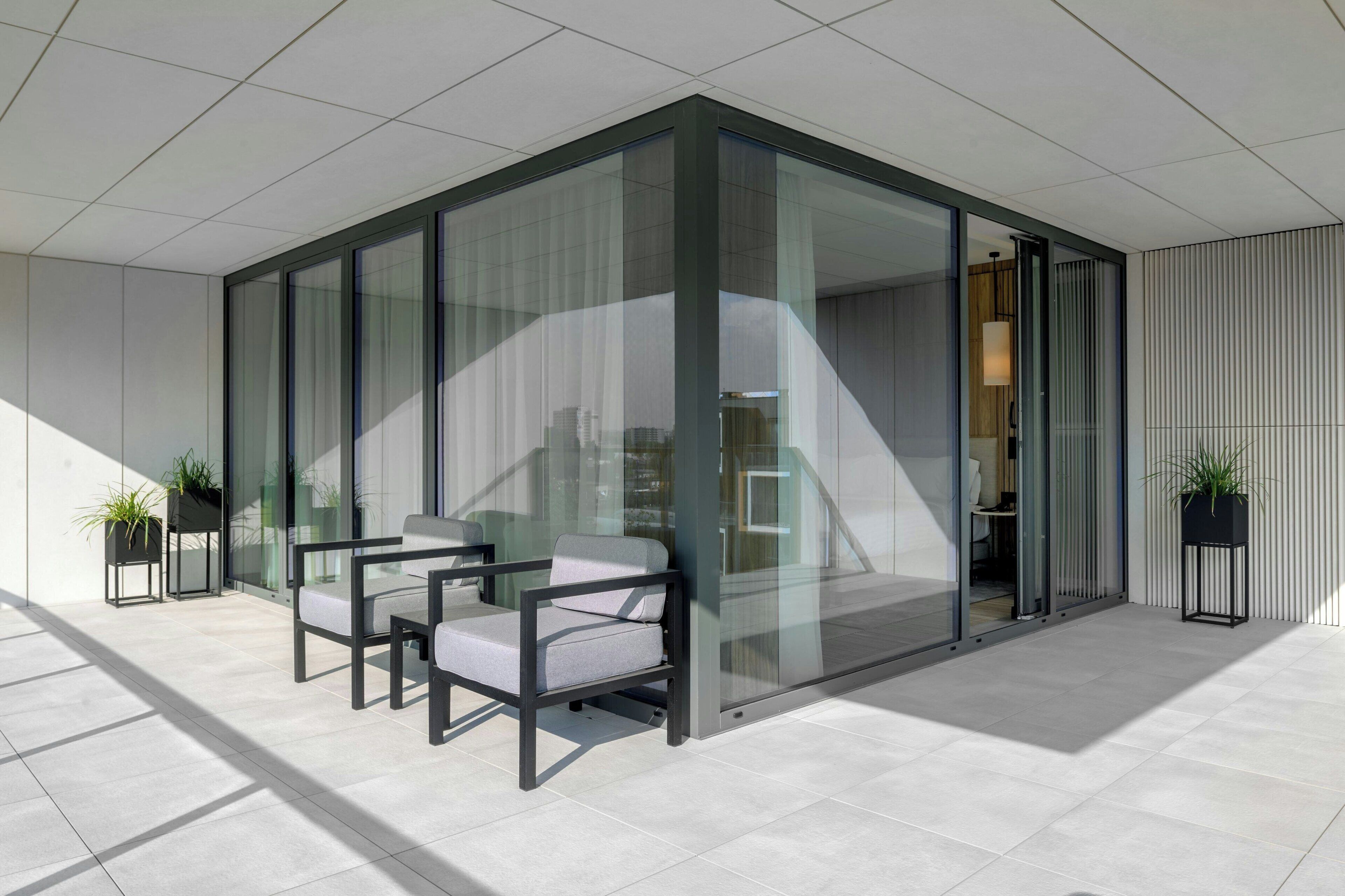 A modern interior with a glass partition, a seating area with two chairs, and a potted plant.