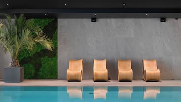 Zona junto a la piscina con cuatro sillones de madera alineados contra una pared, un macetero con planta verde y una pared gris con textura.