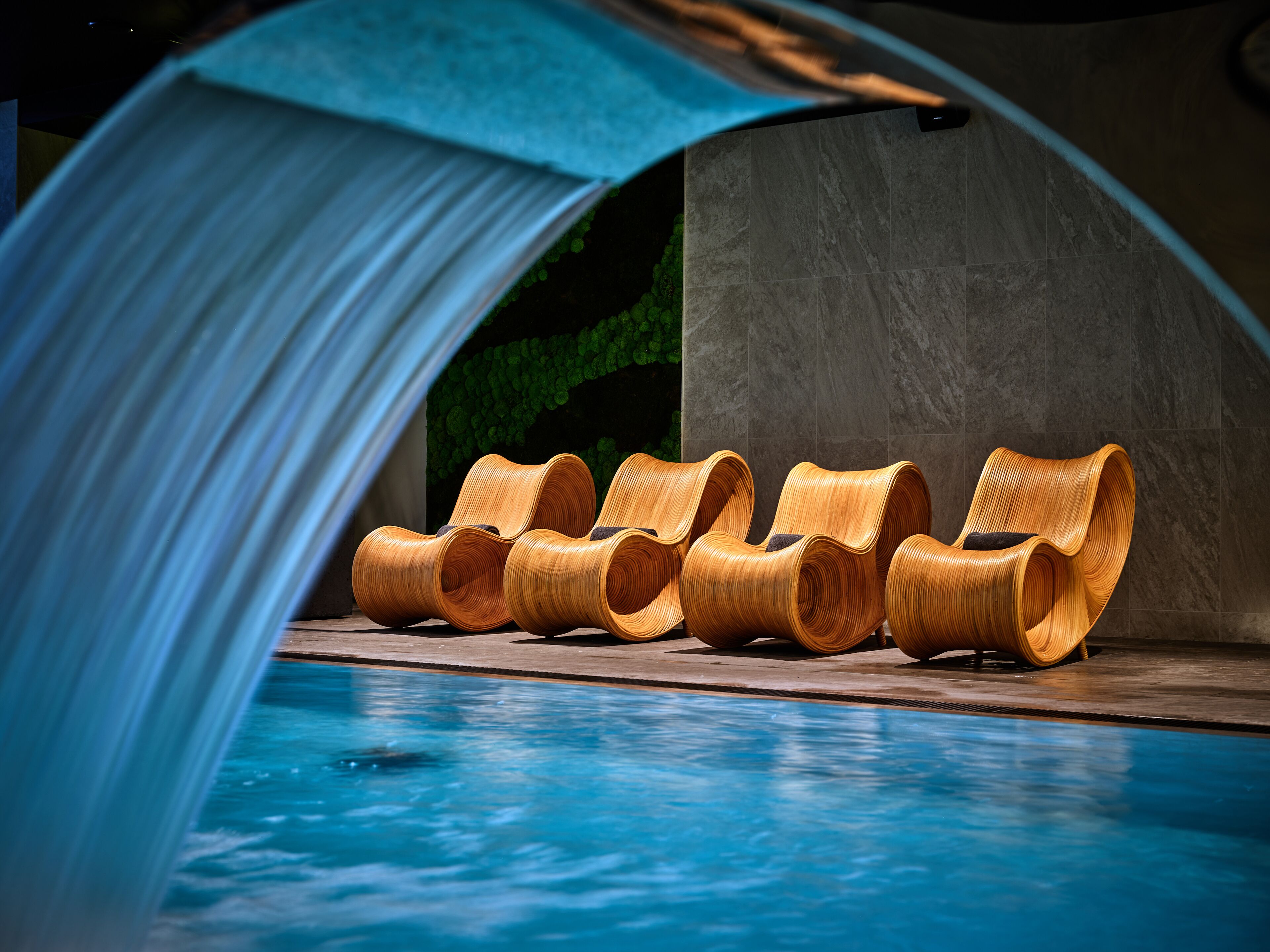 A poolside area with a series of uniquely shaped lounge chairs and a clear blue pool.