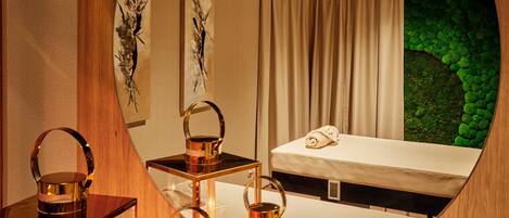 A modern bedroom with a round mirror, wooden paneling, a bed, a green moss wall, and candles.