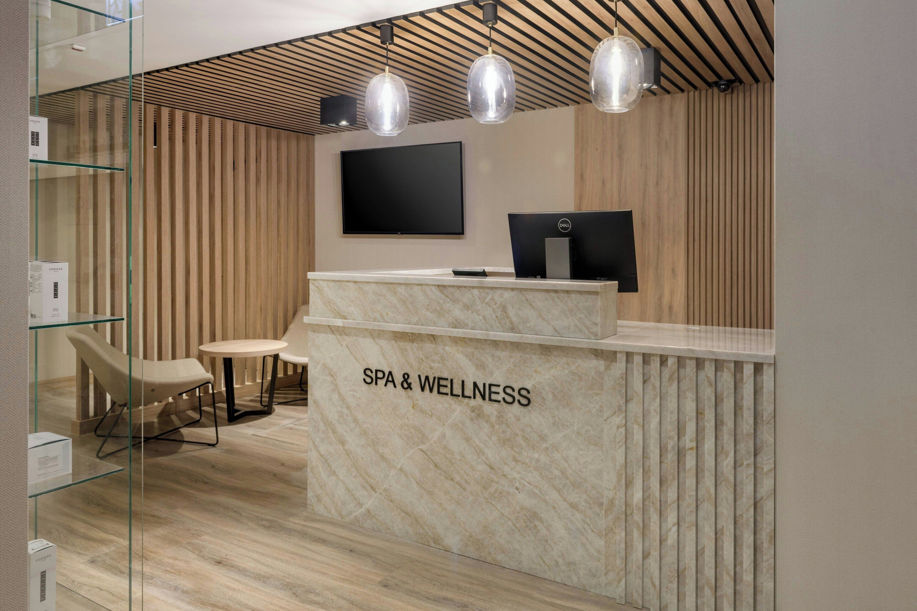 A spa and wellness reception area with a marble counter, two chairs, a flat-screen TV, and pendant lighting.