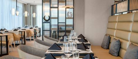 Un comedor moderno con una mesa larga dispuesta para una comida, asientos acolchados e iluminación colgante.