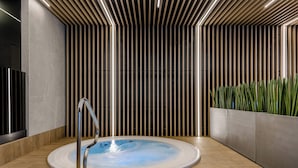 A modern indoor pool area with a circular hot tub, wooden slatted walls, and a wooden floor.