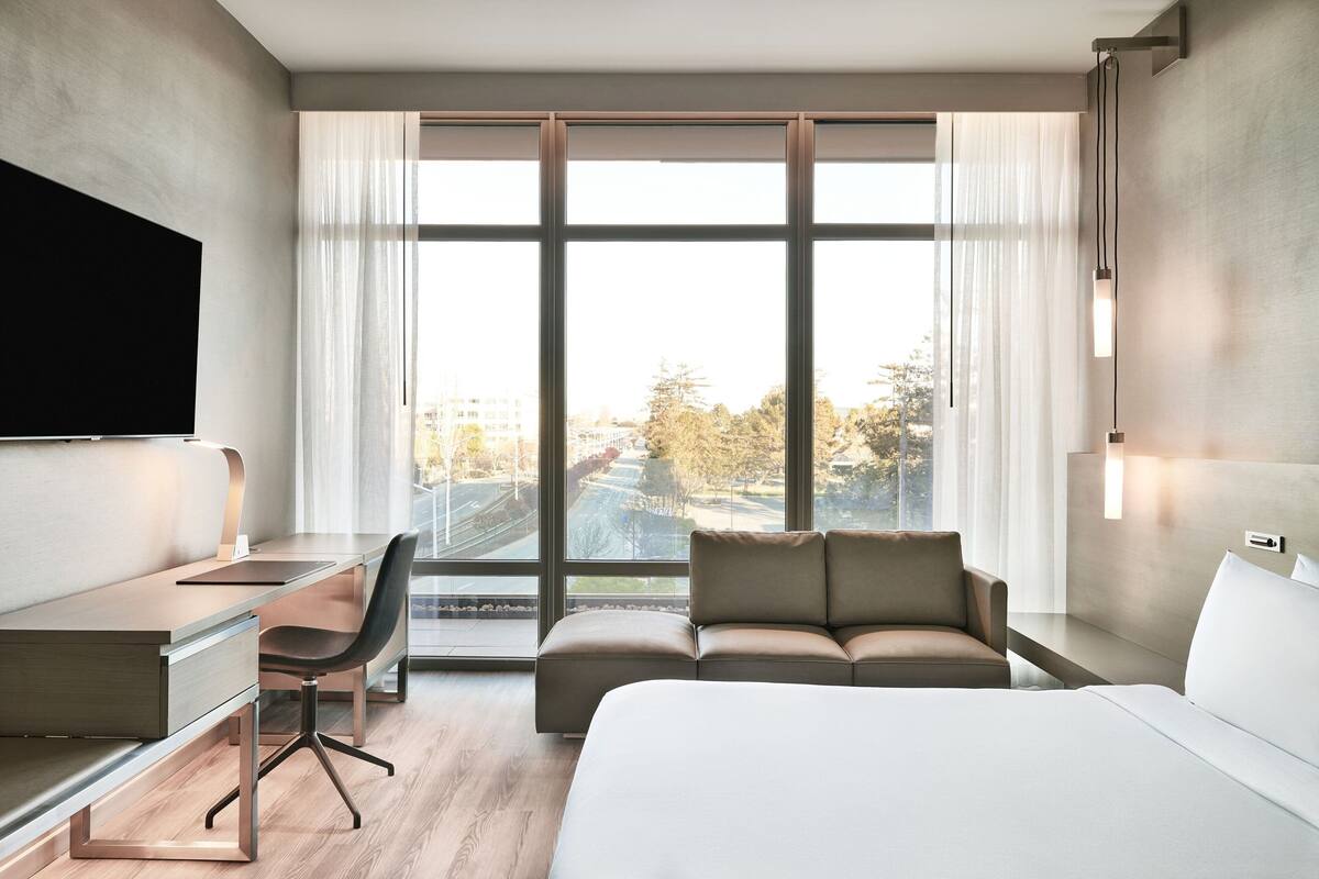 Habitación de hotel moderna con una cama grande, un escritorio, un sofá y un televisor montado en la pared.