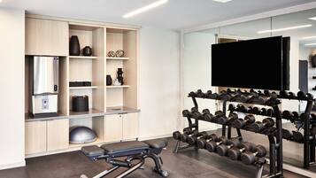 Een moderne sportschool met een tv aan de muur, een dumbbellsysteem, een hometrainer en een koffieapparaat.