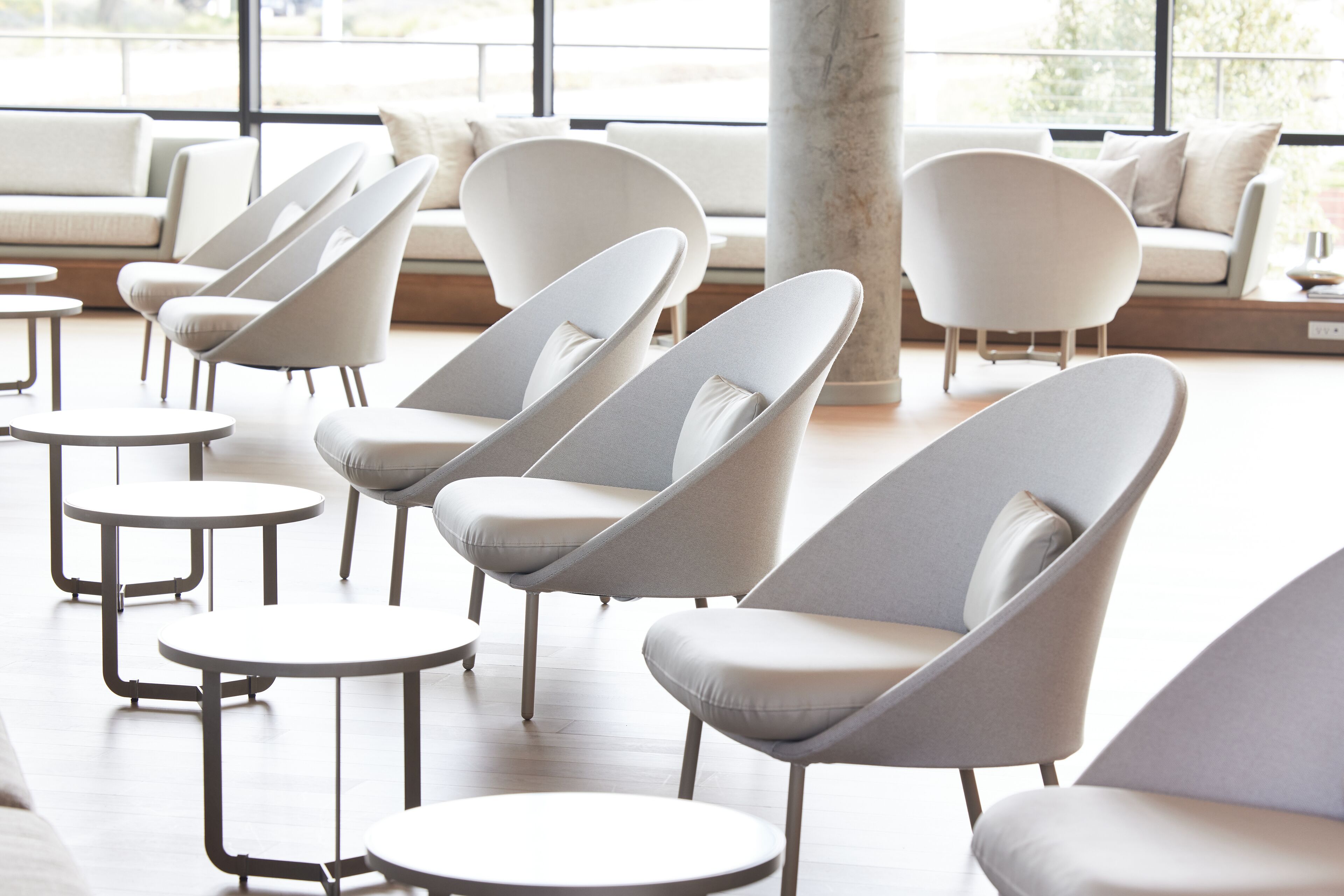 A modern lounge area with multiple seating options including sofas and chairs, arranged around small round tables.