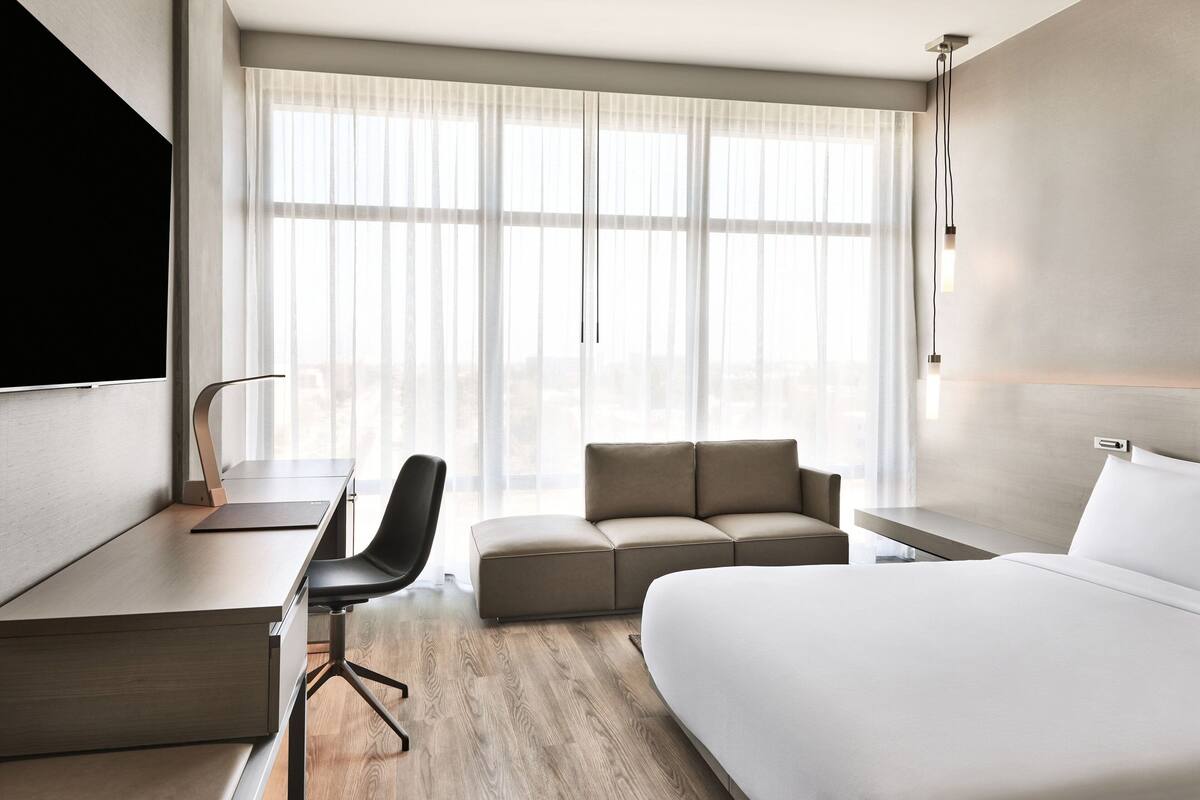 Una habitación de hotel moderna con una cama grande, un escritorio con silla, un sofá y un televisor montado en la pared.