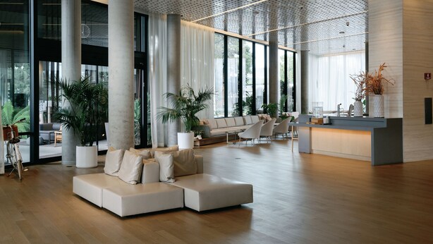 Un hall espacioso con diseño moderno, que incluye un amplio sofá modular, varias zonas de estar y grandes ventanales que dejan entrar luz natural.