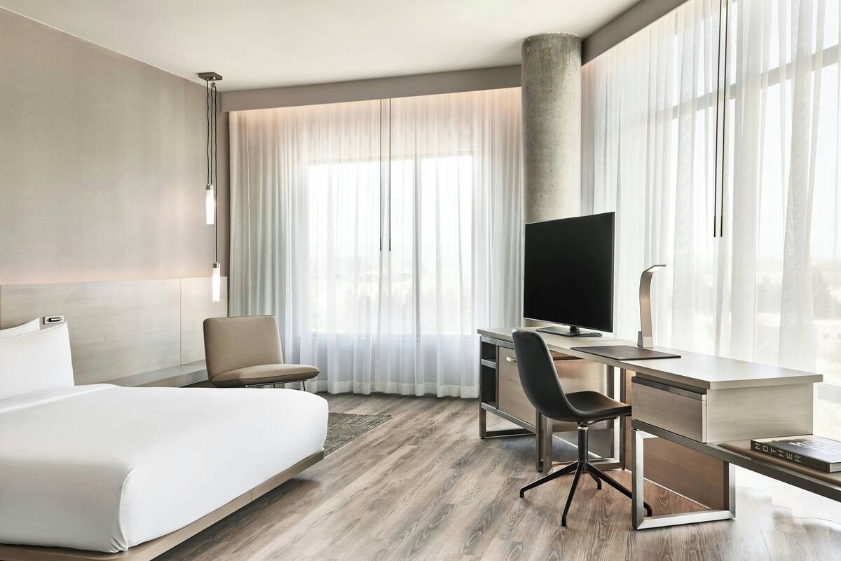 Una habitación de hotel moderna con una cama grande, un escritorio con ordenador, una silla y televisor.
