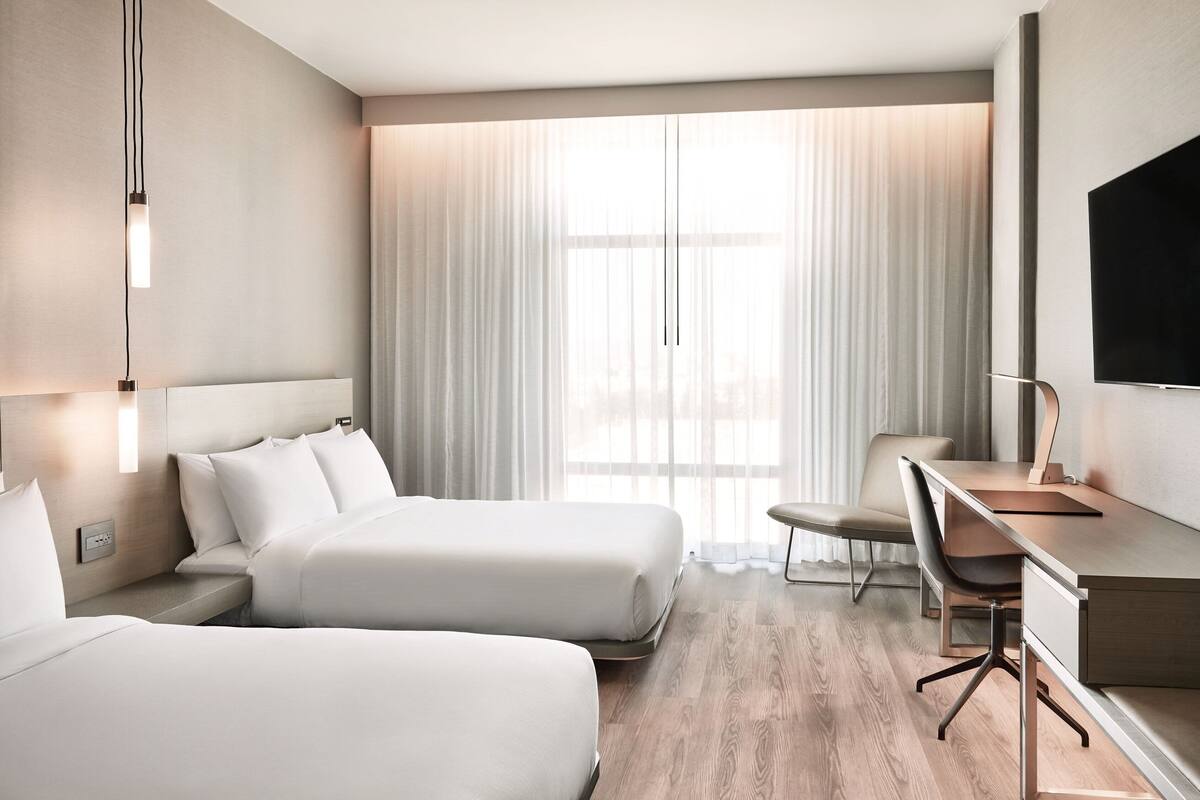 Una habitación de hotel moderna con dos camas, un escritorio y un televisor.