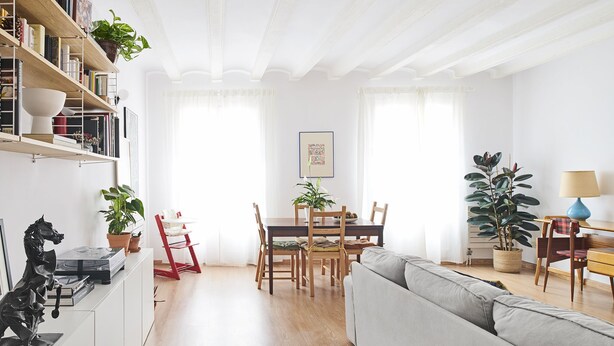 Een moderne woonkamer met een houten eettafel, een grijze bank en een boekenkast vol boeken en decoratieve spullen.
