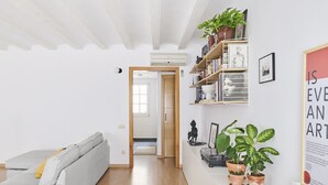 Een moderne woonkamer met een grijze bank, houten vloeren, een boekenkast met planten en een citaat in een lijst op de muur.
