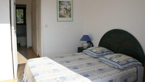 Ein Schlafzimmer mit einem Bett, einem Nachttisch mit Lampe, einem gerahmten Bild an der Wand und einer Tür zu einem weiteren Raum.