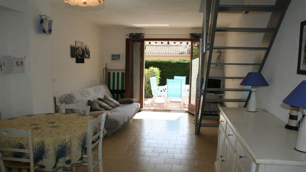 A compact living space with a sofa, dining table, and chairs, a staircase, and a view of the outside.