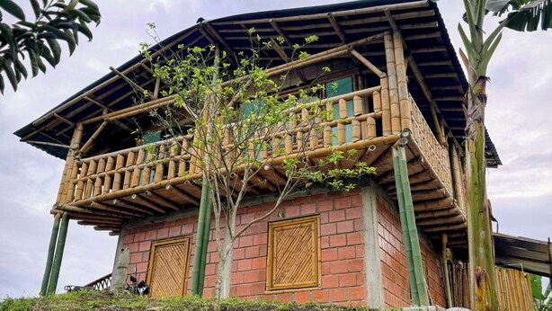 A traditional bamboo structure with a brick base, a wooden balcony, and a large banana tree nearby.
