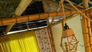 A bed with a patterned quilt, a green pillow, and a hanging lantern in a room with bamboo structures.