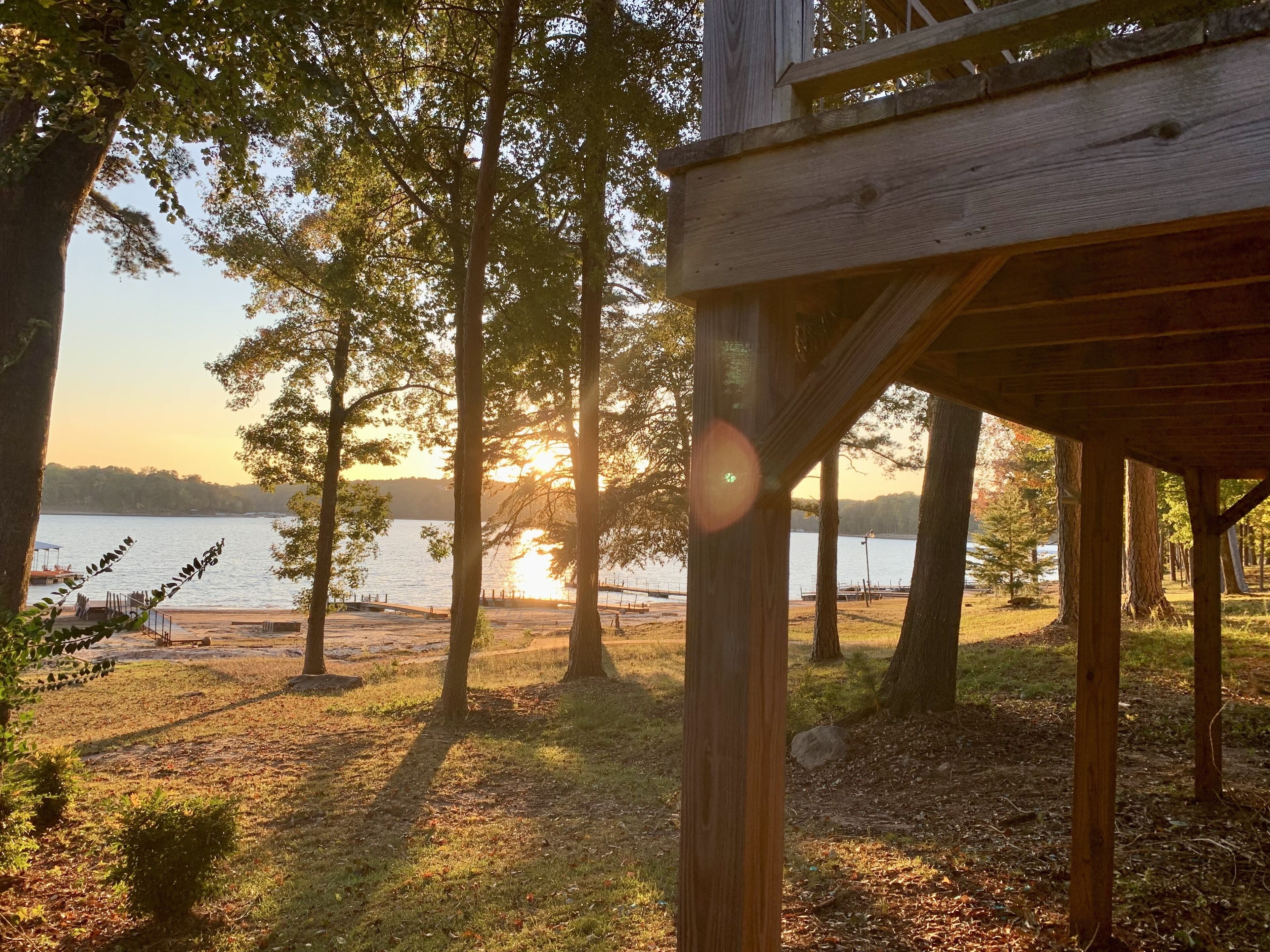 Terraza de madera con vistas a un lago, árboles y un atardecer.