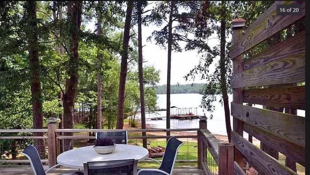 Una terraza de madera con una mesa redonda y sillas, con vistas a un lago.