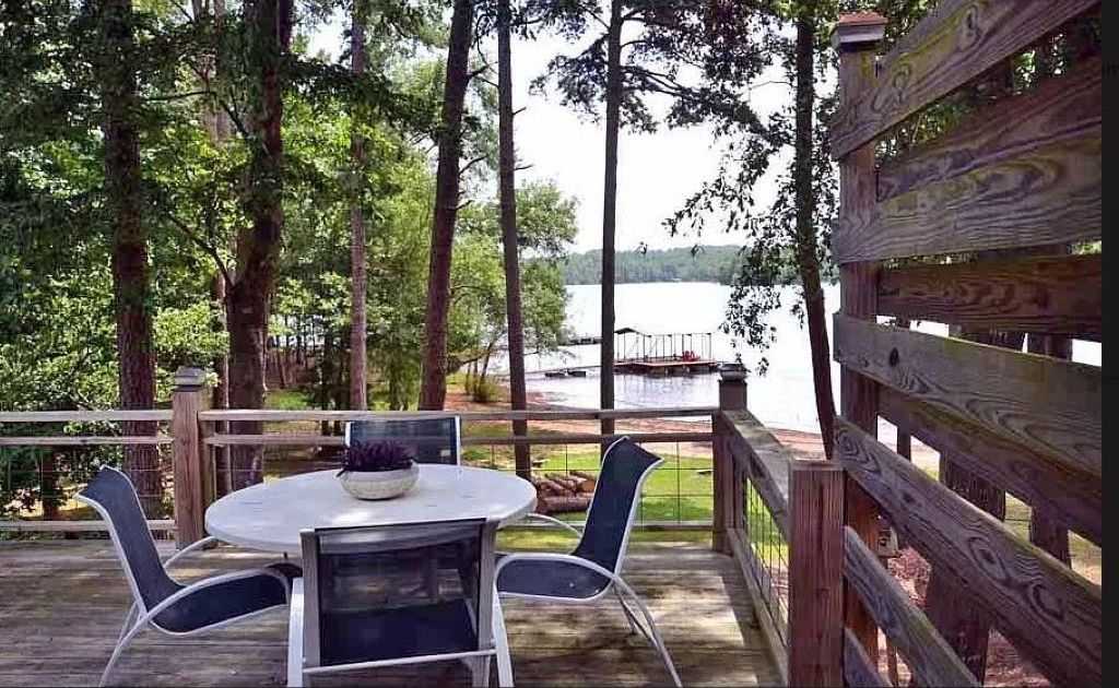 A wooden deck with a round table and chairs, overlooking a lake.