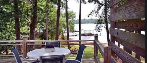 A wooden deck with a round table and chairs, overlooking a lake.