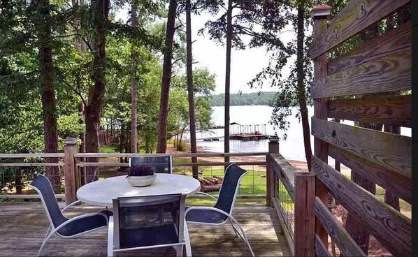 Una terraza de madera con una mesa redonda y sillas, con vistas a un lago.