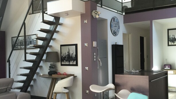 A modern loft apartment with a high ceiling, exposed beams, a staircase, and a dining area with a glass table. - LOFT P'TITE POMME with SPA (Azay-le-Rideau)
