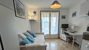 A compact bedroom with a bed, a desk, a chair, a TV, and a fan.