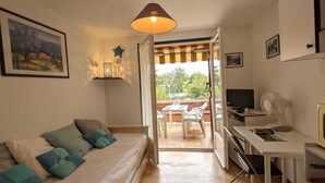A cozy room with a bed, a desk, a TV, and a balcony with a view of greenery.