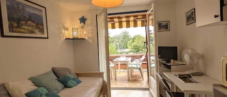 Una habitación acogedora con cama, escritorio, televisión y balcón con vistas a zonas verdes.