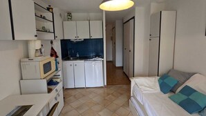 A compact living space with a kitchenette, a bed with blue pillows, and a ceiling light fixture.