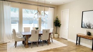 Un comedor con una mesa de madera y seis sillas, una lámpara colgante, una planta en maceta y un cuadro en la pared.