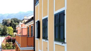 A yellow building with green shutters, a balcony, and a view of a green lawn and trees. - Balcony Condo Steps to Beach & Train Station - O (Levanto)