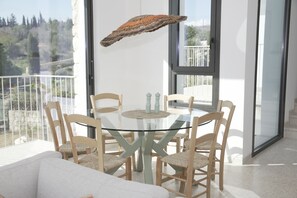 Un comedor moderno con una mesa de vidrio rodeada de sillas de madera, un adorno colgante y vistas a un balcón con barandilla.
