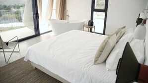 Ein modernes Schlafzimmer mit einem großen Bett, einer freistehenden Badewanne und einem Balkon mit Blick.