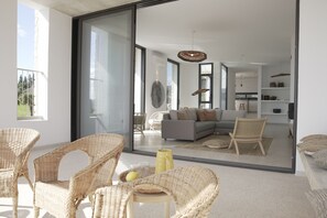 Una sala de estar moderna con muebles de mimbre, un sofá gris y un amplio ventanal corredero que da a un balcón.
