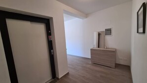 A hallway with a door, a light switch, and a small dresser with a mirror. - Levanto Condo w/ Terrace, Near Beach & Train  P (Levanto)