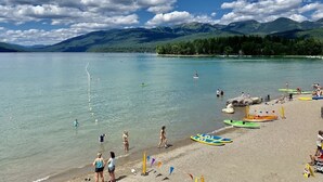 A beach with clear water, people, and mountains in the background.